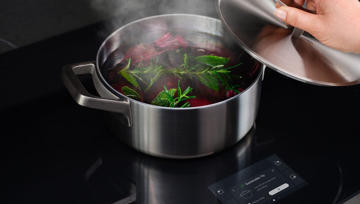 Uma mão a retirar a tampa de uma frigideira com legumes a ferver.