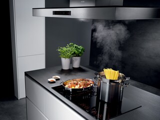 Alimentos a cozinhar numa placa de indução da AEG enquanto um exaustor da AEG extrai o excesso de vapor