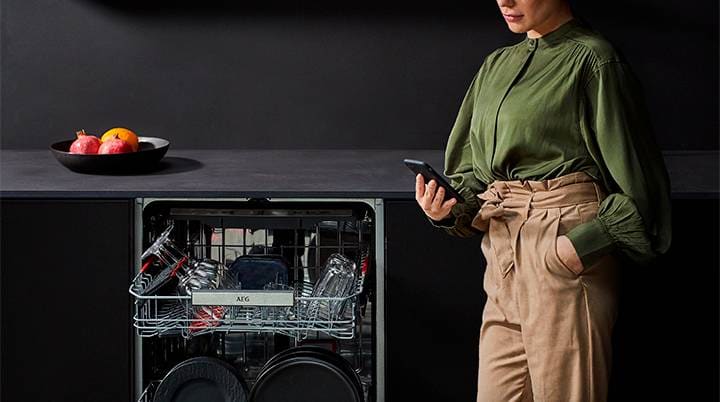 Mulher de blusa verde a usar o telefone ao lado da máquina de lavar loiça