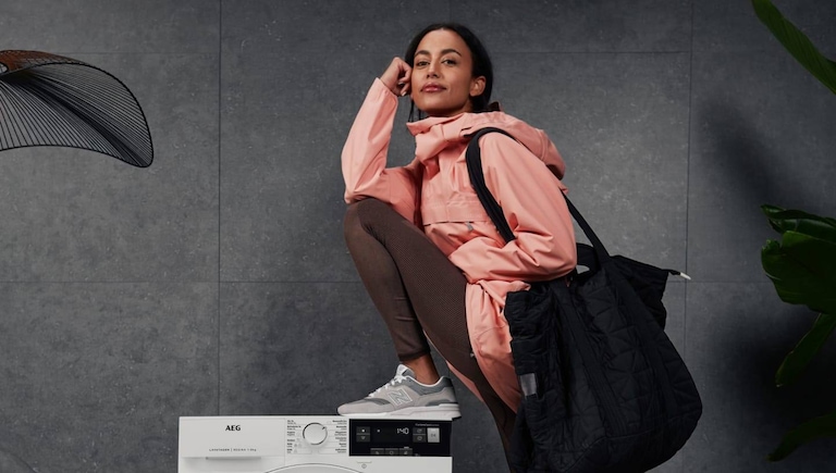 Mulher encostada a uma máquina de lavar e secar AEG.