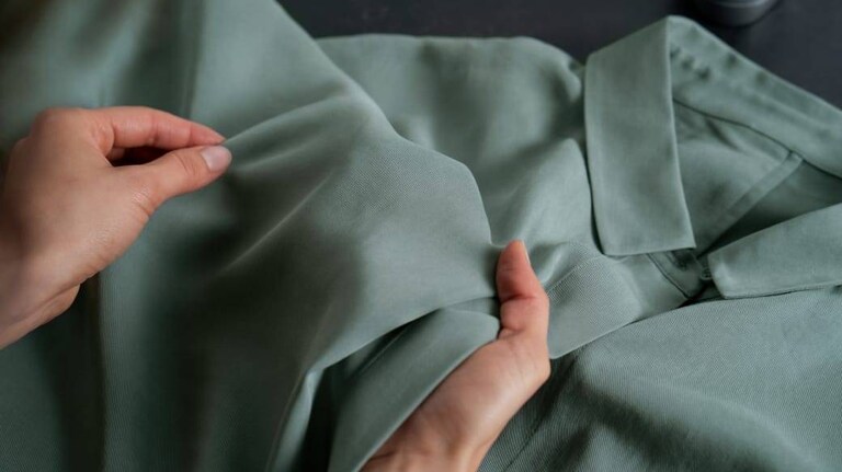 Mãos segurando uma camisa verde para inspeção