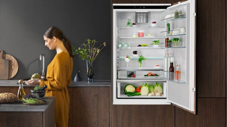 Mulher de pé numa cozinha com a porta do frigorífico aberta